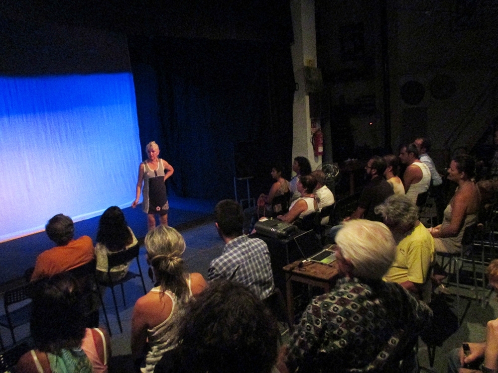 woman on stage in front of a movie screen with audience members visible in front of her